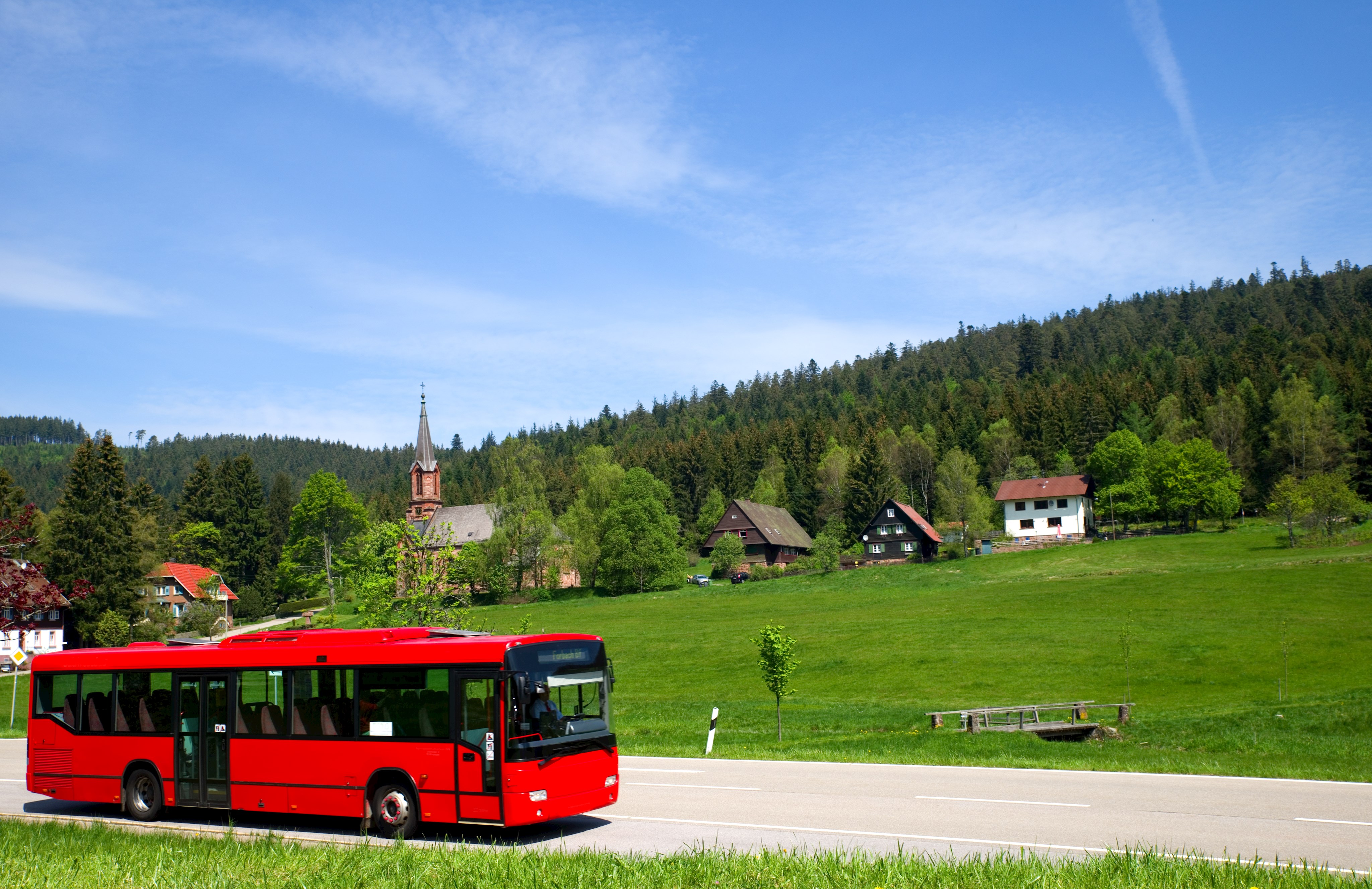 Das Bild zeigt einen roten Bus auf einer Landstraße und steht für öffentlichen Nahverkehr.
